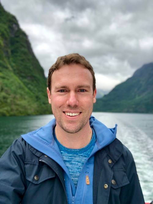 Alumnus Christopher Penzien in front of a body of water in a mountainous valley